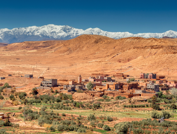 Panorama sur les montagnes de l’Atlas enneigées dominant un village marocain traditionnel au milieu du désert, Maroc